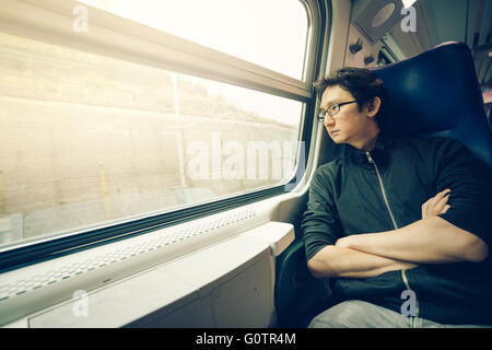 Handsome asian man looking through train window, warm light tone, with copy space