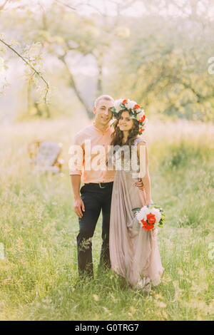 Beautiful romantic couple  standing holding hands in garden, wooden chair on background Stock Photo