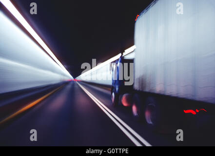 Blur pan action view of tractor trailer truck speeding through underground mountain tunnel Stock Photo