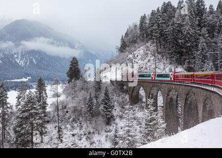 Famous sightseeing train running over viaduct in Switzerland, the Glacier Express in winter Stock Photo