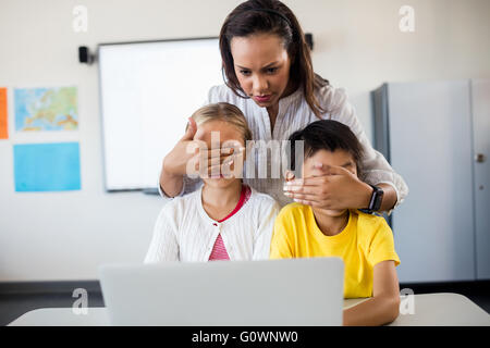 Teacher covering pupils eyes in front of computer Stock Photo
