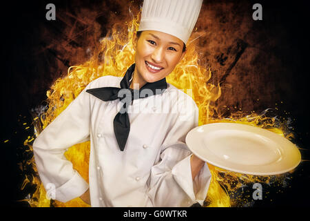 Composite image of smiling female cook holding empty plate in kitchen Stock Photo