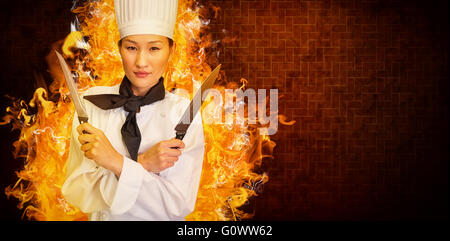 Composite image of confident female cook holding knives in kitchen Stock Photo