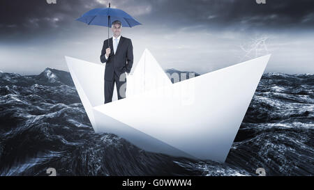 Composite image of businessman smiling at camera and holding blue umbrella Stock Photo