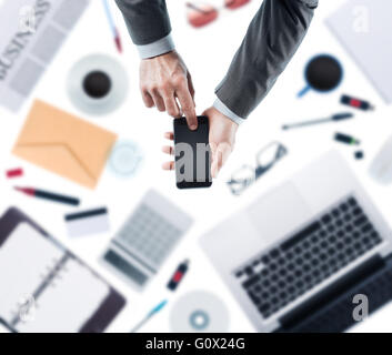 Businessman using a touch screen smartphone, desktop with laptop on background, top view Stock Photo