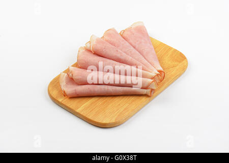 rolled ham slices on wooden cutting board Stock Photo