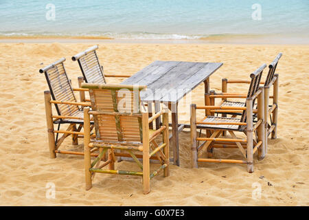 Wooden bamboo furniture, table and five chairs around on san beach with blue sea water background Stock Photo