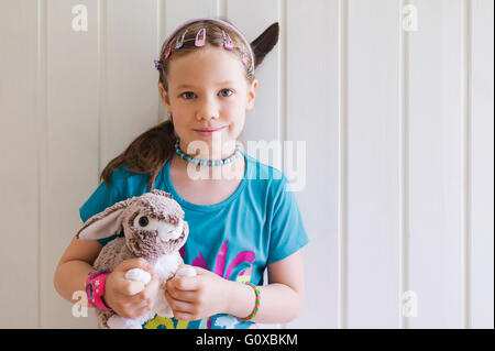 Portrait of young girl standing in front of wall holding her toy bunny, Sweden Stock Photo