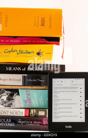 Amazon Kindle turned on leaning against stack of paperback books with titles, to show the amounts of reading material that can fit a electronic reader. Stock Photo