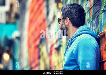 Profile of a stylish handsome guy wearing sunglasses and casual clothing standing near beautiful colorful city wall background Stock Photo