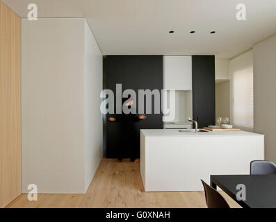 Open plan kitchen and dining area with modern furniture and features. Blurred view of woman in background. Stock Photo