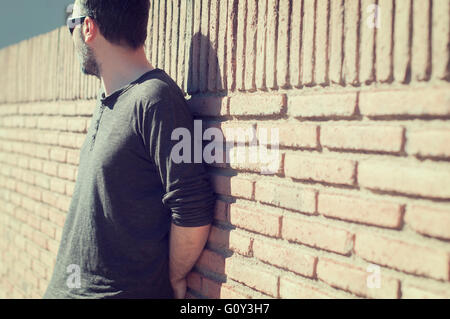 A man wearing sunglasses leaning against a wall Stock Photo - Alamy