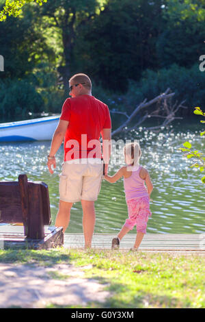 Father and daughter standing by riverbank holding hands Stock Photo