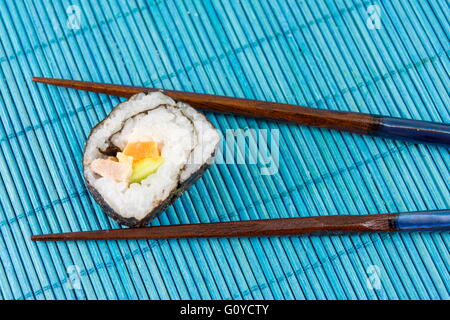 Sushi roll caught by chopsticks on blue bamboo background Stock Photo