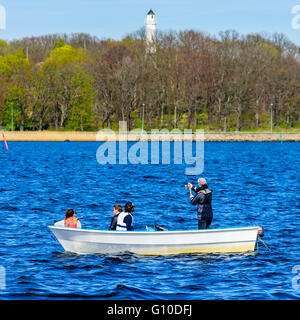 Karlskrona, Sweden - May 03, 2016: Four persons in a small open motorboat fishing at sea with coastline and lighthouse in backgr Stock Photo