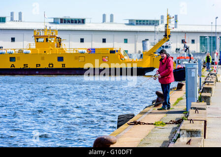 Karlskrona, Sweden - May 03, 2016: Senior male angler standing dockside in front of a car ferry fishing for herring. Real people Stock Photo