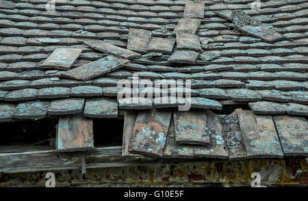 A decrepit old house with a damaged and devastated roof and tiles. Stock Photo