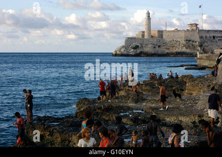 Local people along the famous Malecon on the waterfront in the Old City of Havana. Castillo de los Tres Reyes del Morro, Havanna, Cuba, Caribbean Stock Photo