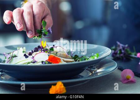 Chef in hotel or restaurant kitchen cooking, only hands. He is working on the micro herb decoration. Stock Photo