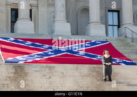 Columbia, South Carolina, USA. 07th May, 2016. A University of South Carolina graduate still in cap and gown has his photo taken in front of a giant Confederate Battle flag on the steps of the State House placed for Confederate Memorial Day celebrations May 7, 2016 in Columbia, South Carolina. The events marking southern Confederate heritage come nearly a year after the removal of the confederate flag from the capitol following the murder of nine people at the historic black Mother Emanuel AME Church. Credit:  Planetpix/Alamy Live News Stock Photo