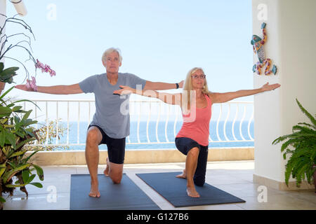 Senior man and woman exercising yoga on the balcony of their ocean front home Stock Photo