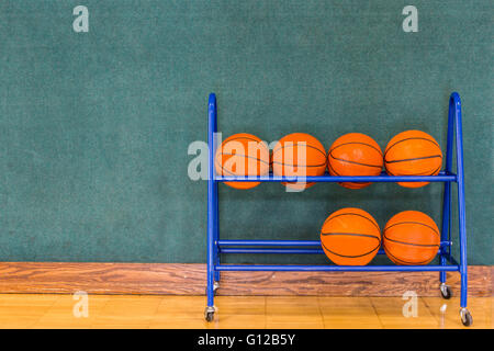 Basketballs stored in a rack up against a wall on a gym or court floor.  Copy space. Stock Photo