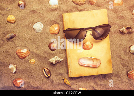 Reading favourite old book on summer vacation beach holiday, top view of a book and sunglasses in warm beach snow. Stock Photo