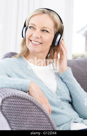 Mature Woman Listening To Music On Wireless Headphones Stock Photo