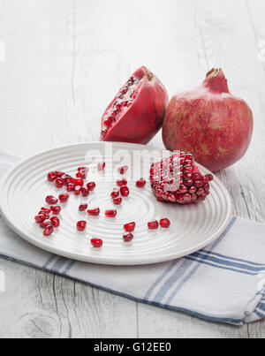 Pomegranate whole, half and seeds on white plate. Vertical image with back lighting. Shallow depth of field. Stock Photo