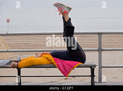 An older woman does stretching and core strengthening exercises on the boardwalk in Brighton Beach, Brooklyn, New York Stock Photo
