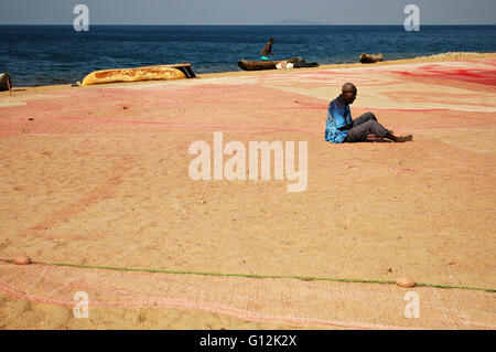Aged african man mending a fishing net on the beach at Cape Maclear, Malawi Stock Photo