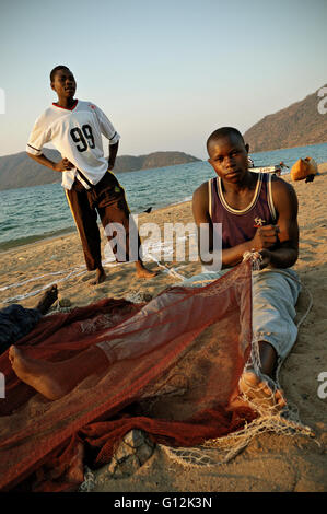 Young man mending a fishing net on the beach in Chembe village, Cape Maclear, Malawi Stock Photo