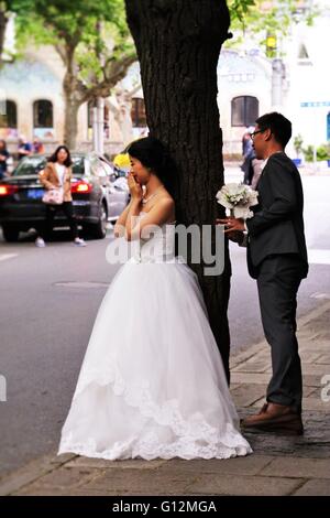 Cute bride leaning on the tree trunk and groom hiding behind the tree in French concession in Shanghai, China. Stock Photo