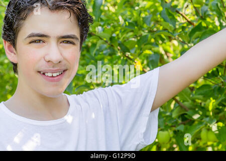 teenager next to rows of apple trees stretches out his hand to show a green apple Stock Photo