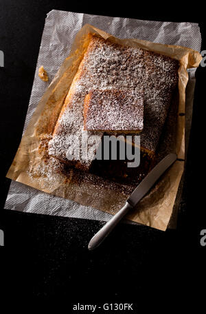 almond cake just baked with powdered sugar on a black stone kitchen table. Northern light effect in a low key Stock Photo