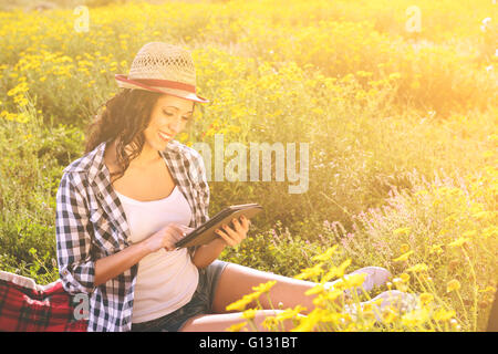 Slim girl in jeans and a T-shirt reading a book in a park sitting on a blanket Stock Photo