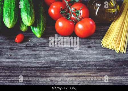 Fresh tomatoes on vine, cucumbers, dry pasta, olive oil and spices on wooden backdrop. Copy space for text Stock Photo