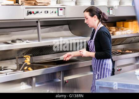 A woman tips cooked chips into a dispenser in a fish and chip shop Stock Photo