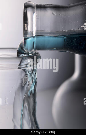 Blue chemistry being poured into Erlenmeyer flask, boiling flask in background Stock Photo