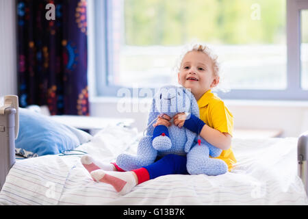 Little boy playing with his toy in bed in hospital room. Child with IV tube and pulse oximeter in modern clinic. Stock Photo