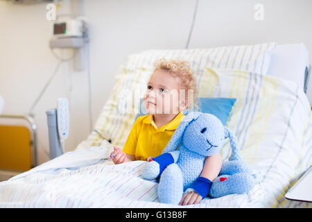 Little boy playing with his toy in bed in hospital room. Child with IV tube and pulse oximeter in modern clinic. Stock Photo