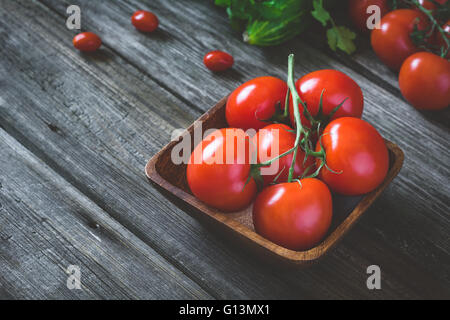 Fresh tomatoes on vine in bowl on rustic wooden table. Selective focus, toned image Stock Photo