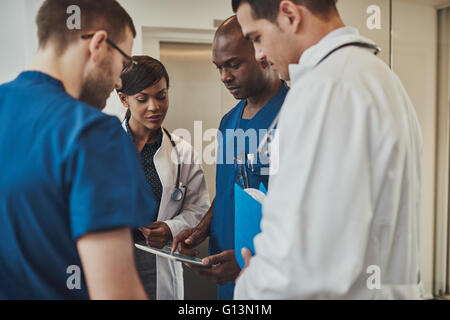Diverse group of multiracial doctors having an emergency discussion standing grouped closely together looking at a handheld tabl Stock Photo