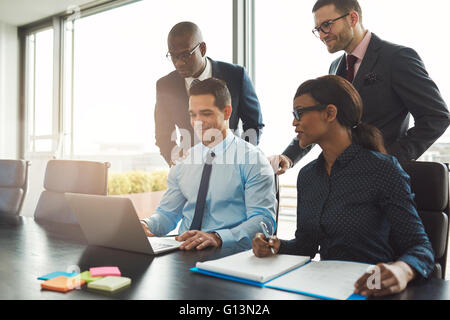Group of happy diverse male and female business people in formal gathered around laptop computer in bright office Stock Photo