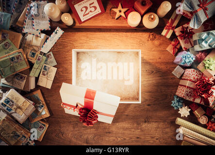 Open empty Christmas gift box on a wooden desktop surrounded by letters and presents, top view Stock Photo