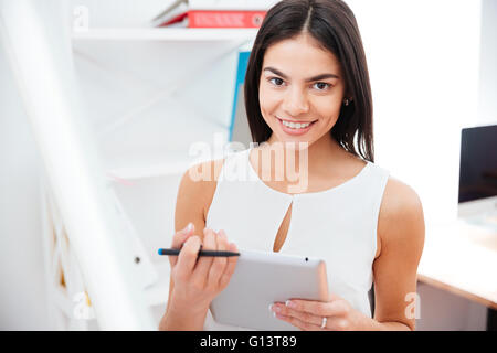 Happy businesswoman holding tablet computer in office and looking at camera Stock Photo