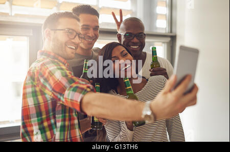 Friends at work taking self portrait with camera phone while holding green glass bottles of beer in office party Stock Photo