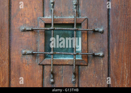 Small square window with grate in old style wooden door, confinement concept Stock Photo