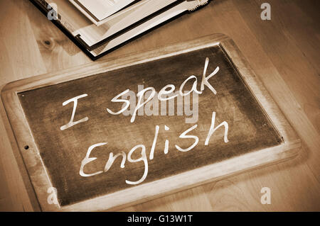 sentence I speak english written with chalk on a blackboard, on a table with books Stock Photo