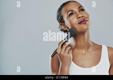 Beautiful young woman with perfect skin applying makeup with a brush against a gray background Stock Photo